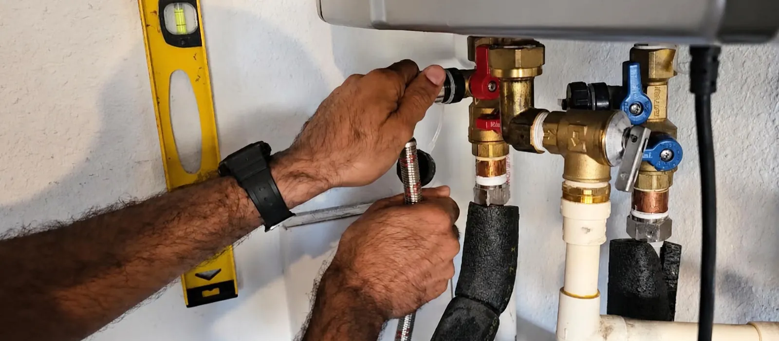 Hands fitting service valves beneath a tankless water heater